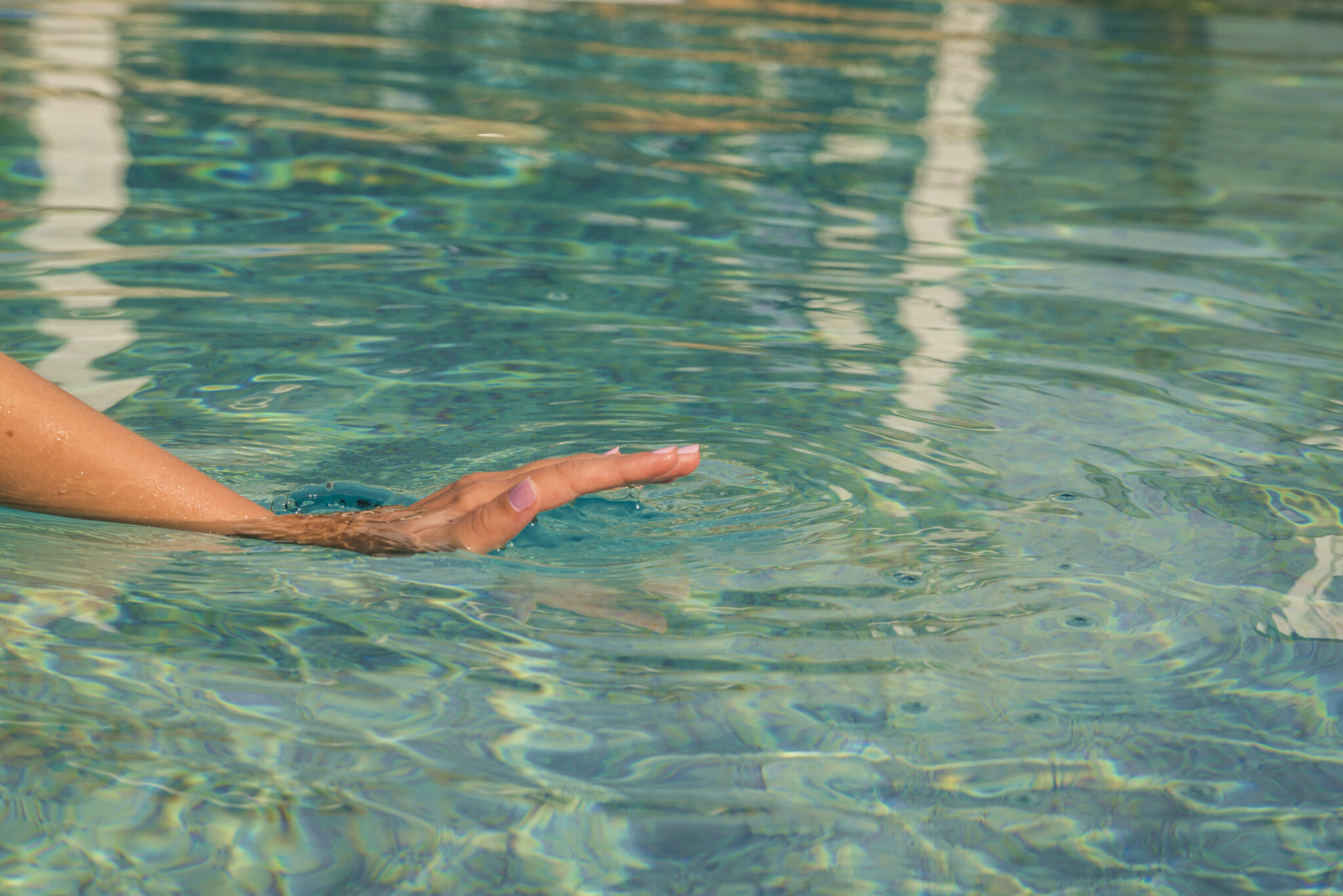 Young woman kneeling by the edge of a swimming pool, touching the calm water with her hand.